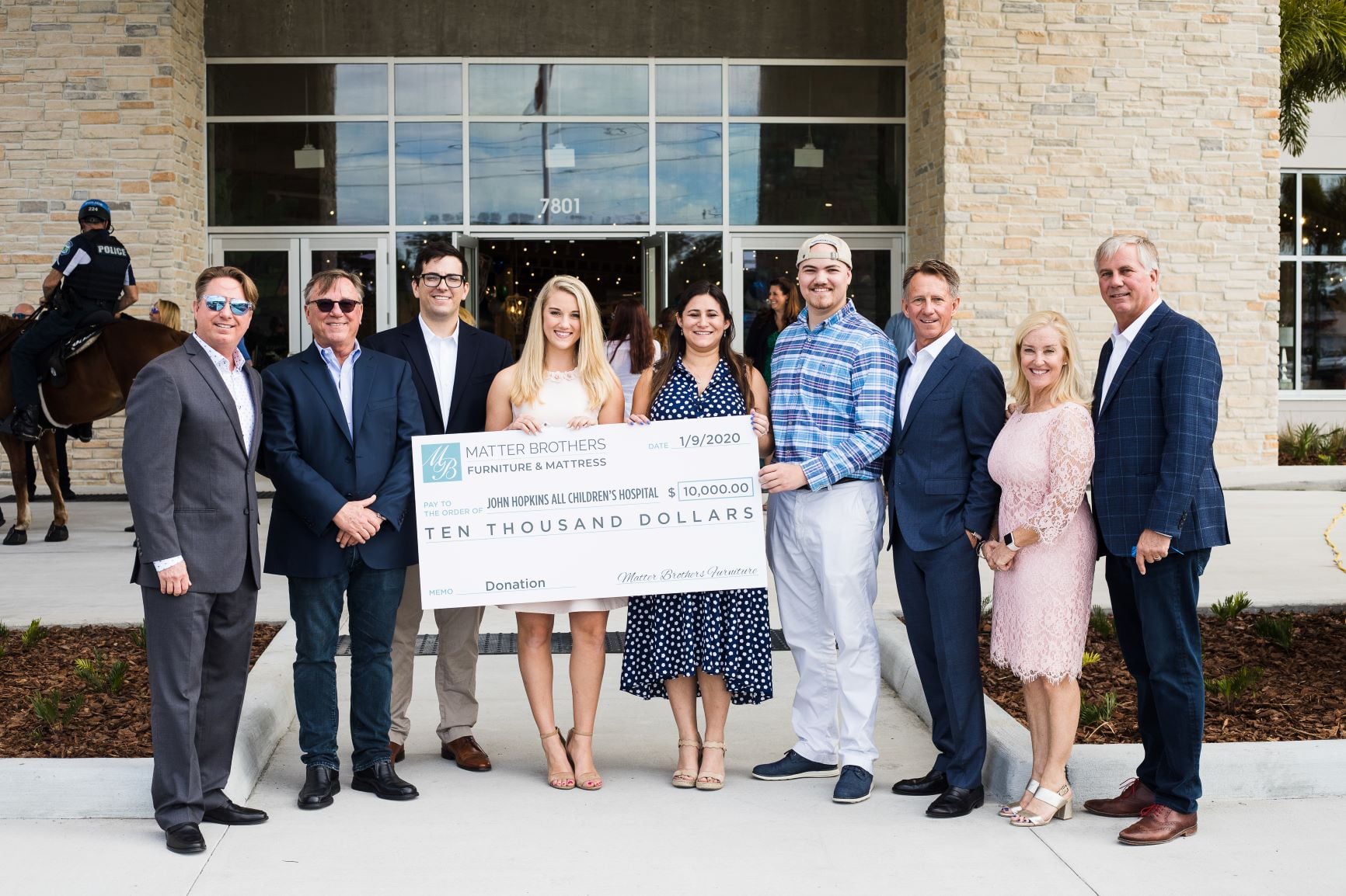 A group of people standing outside a building holding a large check for ten thousand dollars from Matter Brothers Furniture to John Hopkins All Children's Hospital